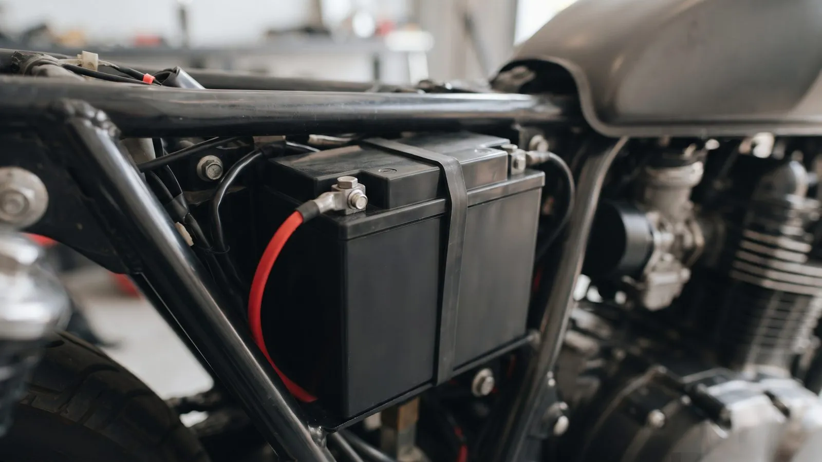 Bateria de moto presa por uma cinta de borracha no quadro, com o cabo vermelho ligado ao polo positivo, numa oficina